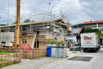 Im Bau befindliches Haus mit Gerüst, Kran und Lkw in der Nähe.