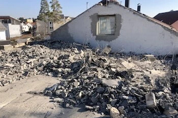 Teilweise abgerissenes Haus mit Betontrümmern davor.