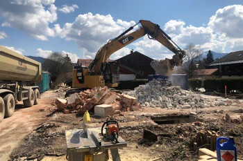 Bagger lädt Schutt auf Lkw an Baustelle unter Wolken.