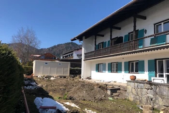 Weißes Haus, blaue Fensterläden; Hof mit Erdhaufen und Schneeflecken.