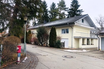 Hellgelbes Haus mit Bäumen an einer kurvigen, ruhigen Straße.
