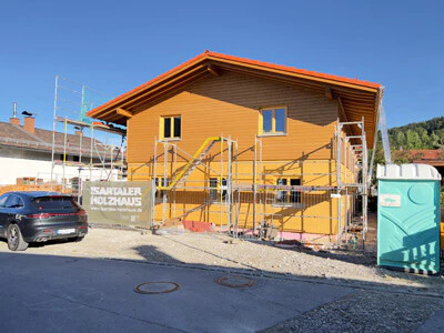 Holzhaus im Bau mit Gerüst, Auto und Dixi-Klo daneben.