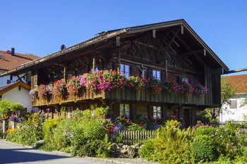 Holzhaus mit Blumenbalkonen und Garten unter blauem Himmel.