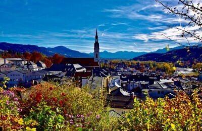 Stadt, Kirchturm, bunte Blumen und Berge bei blauem Himmel.