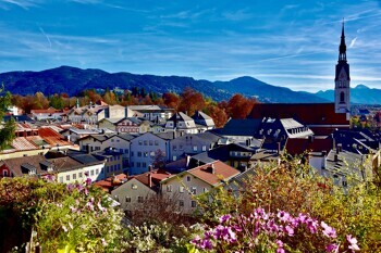 Bunte Stadt mit Kirche, Blumen vorne, Berge im Hintergrund.