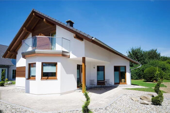 Weißes Haus mit Balkon, großen Fenstern und gepflegtem Garten.