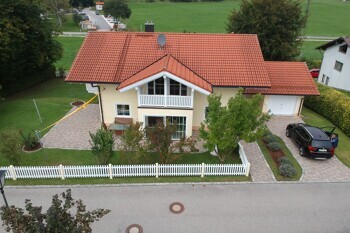 Gelbes Haus mit rotem Dach, weißem Zaun und schwarzem Auto.