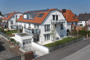 Weiße Doppelhäuser mit roten Dächern, Balkonen und Zäunen bei Sonne.