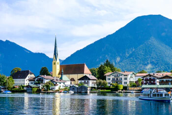 Dorf am See, Kirche, bunte Häuser, Berge, sonniger Tag.