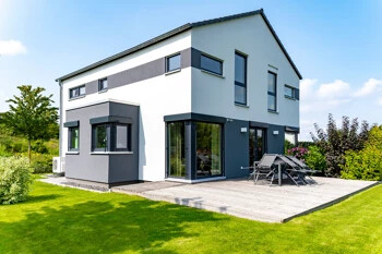 Zweistöckiges Haus mit großen Fenstern, Terrasse und Rasen.
