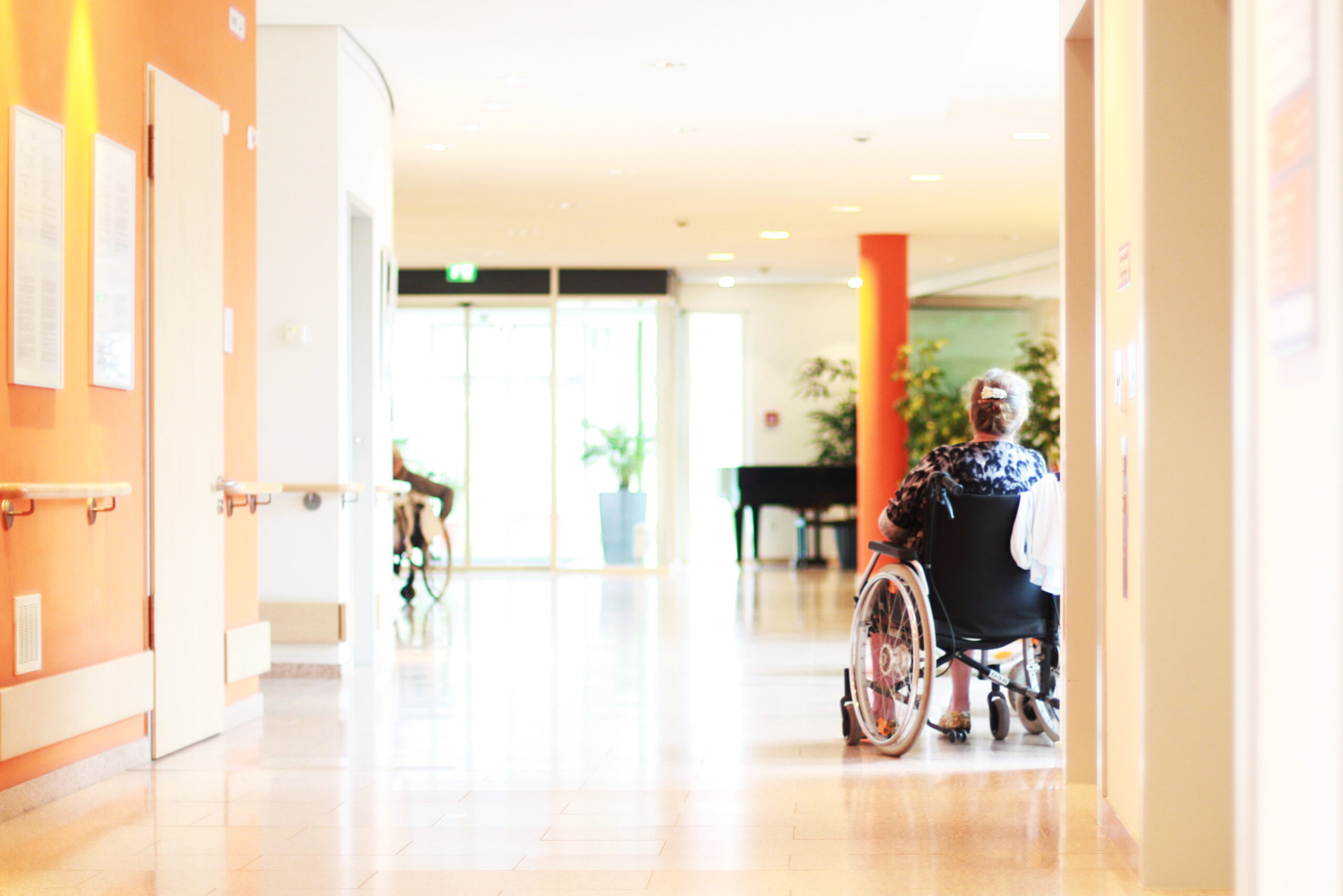Frau Im Rollstuhl in einem Aufenthaltsraum in einem Pflegeheim: Pflegeimmobilien als Kapitalanlage