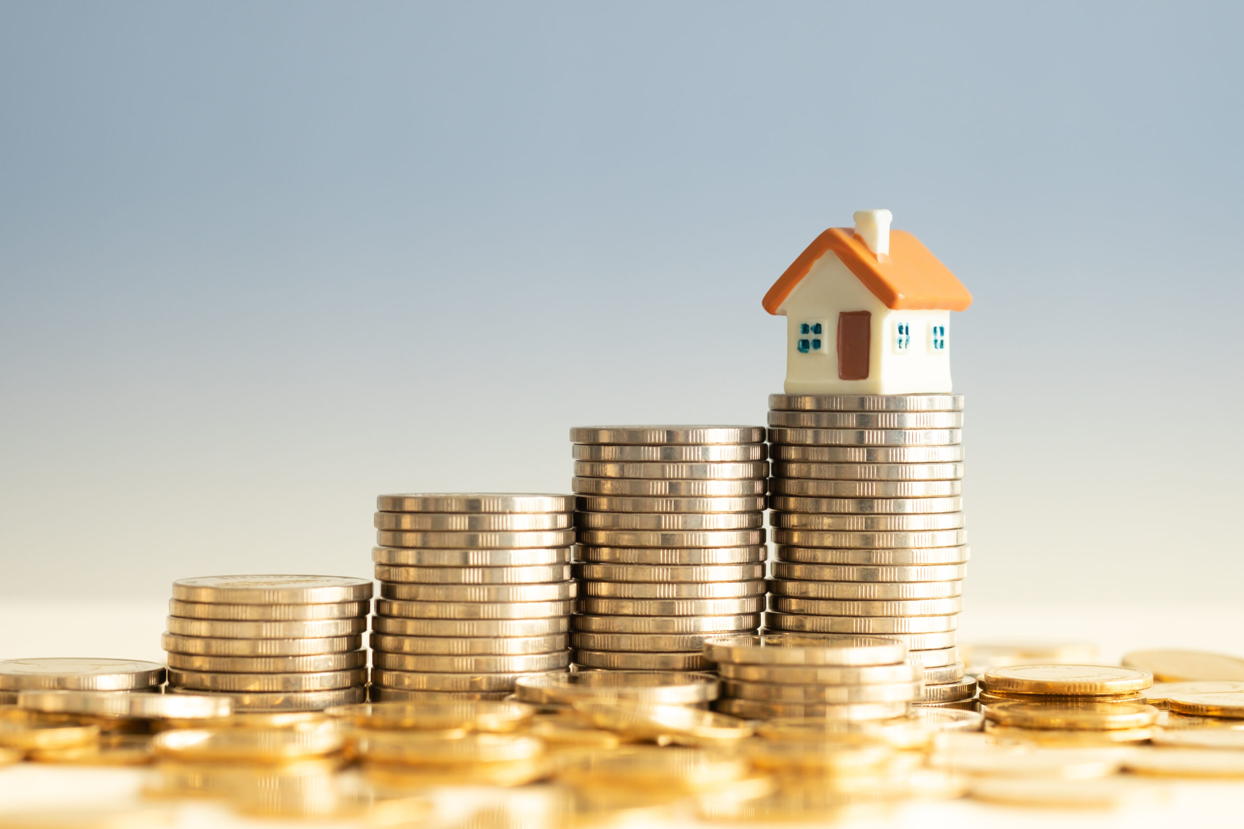 Fünf unterschiedlich hohe Münzstapel stehen nebeneinander, auf dem höchsten Stapel steht ein Modellhaus.