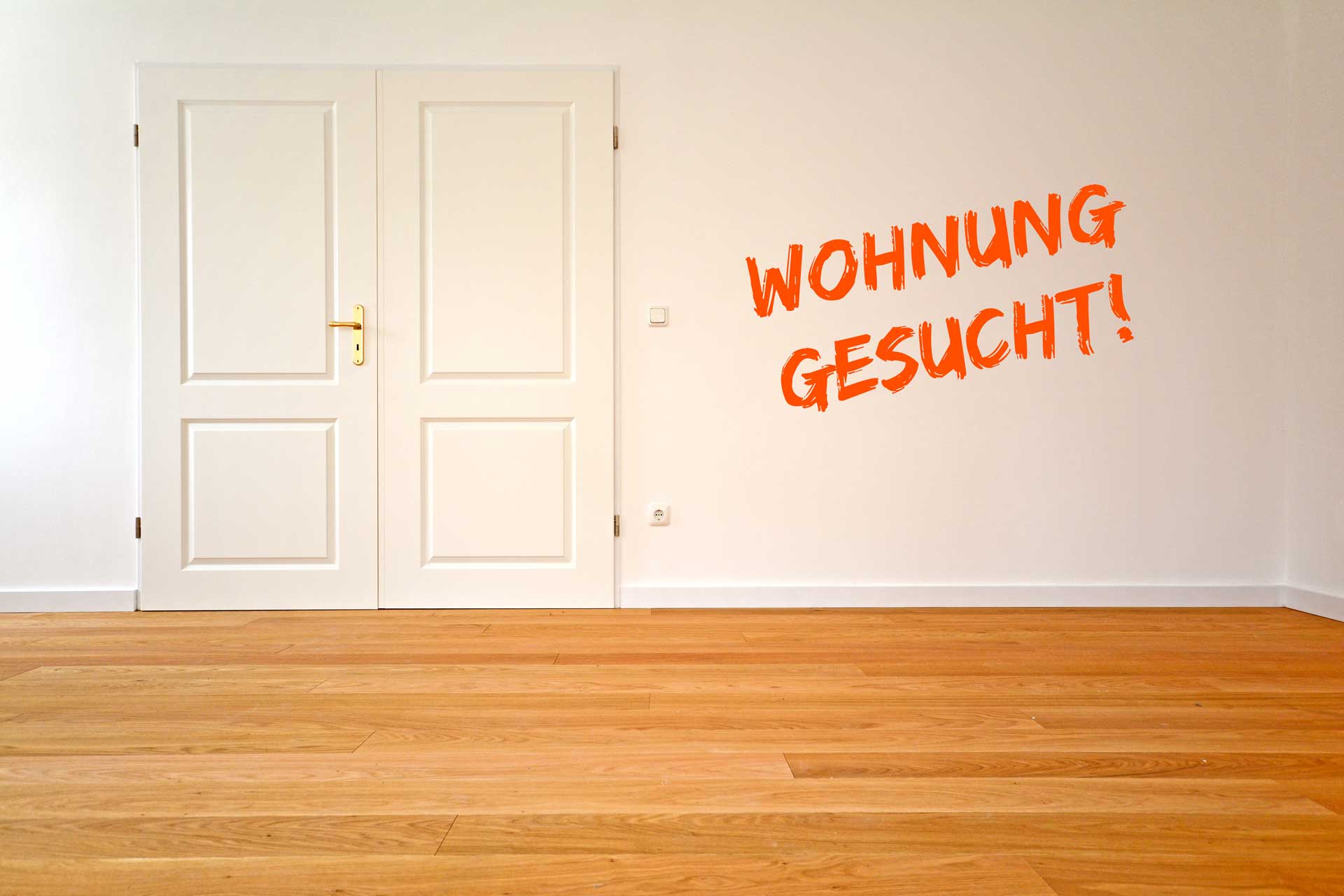 Leeres Zimmer mit orangefarbenem Schriftzug 'Wohnung gesucht' auf weißer Wand, Symbol für Wohnungsnot