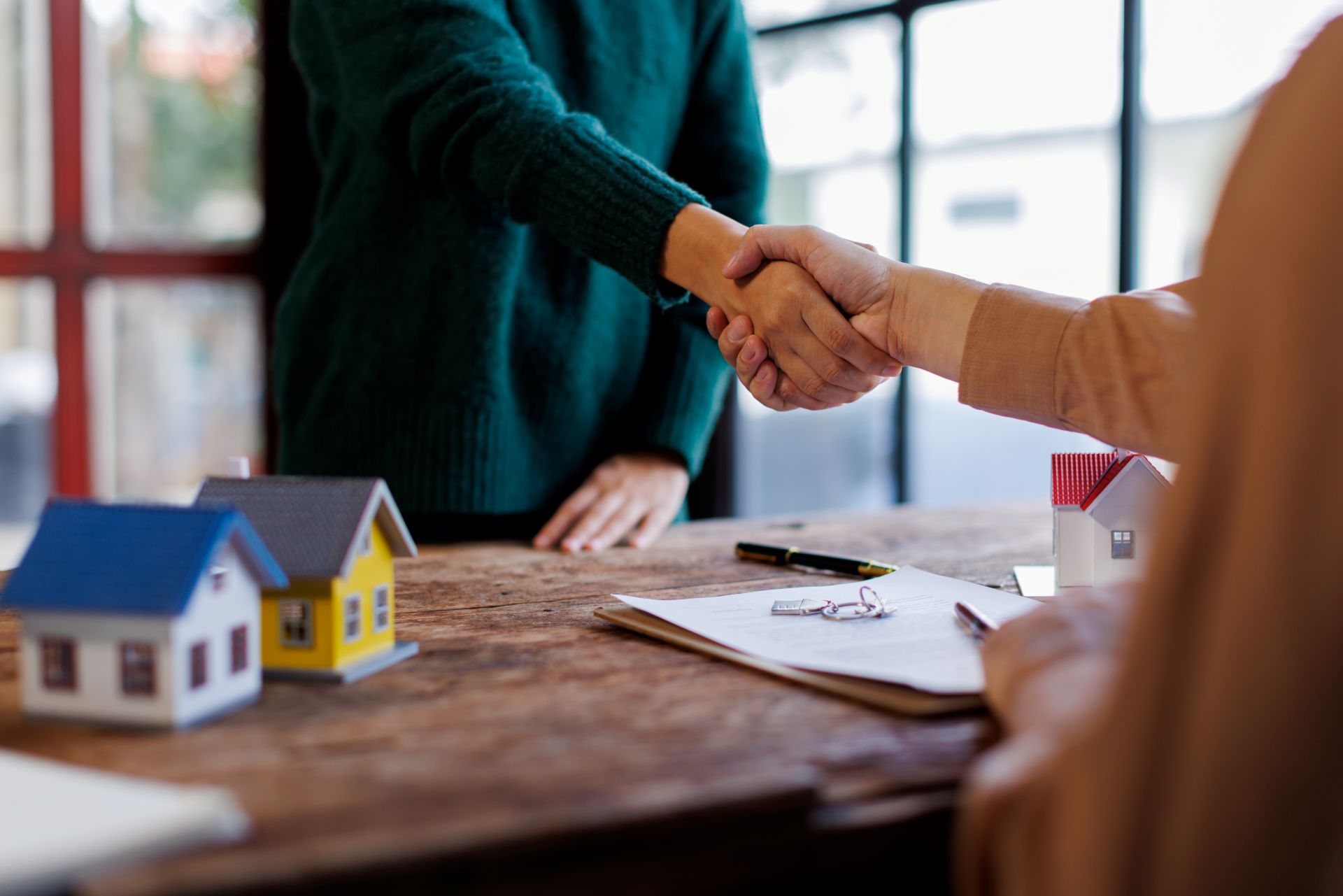 Zwei Personen geben sich am Schreibtisch die Hand, Immobilienvertrag.