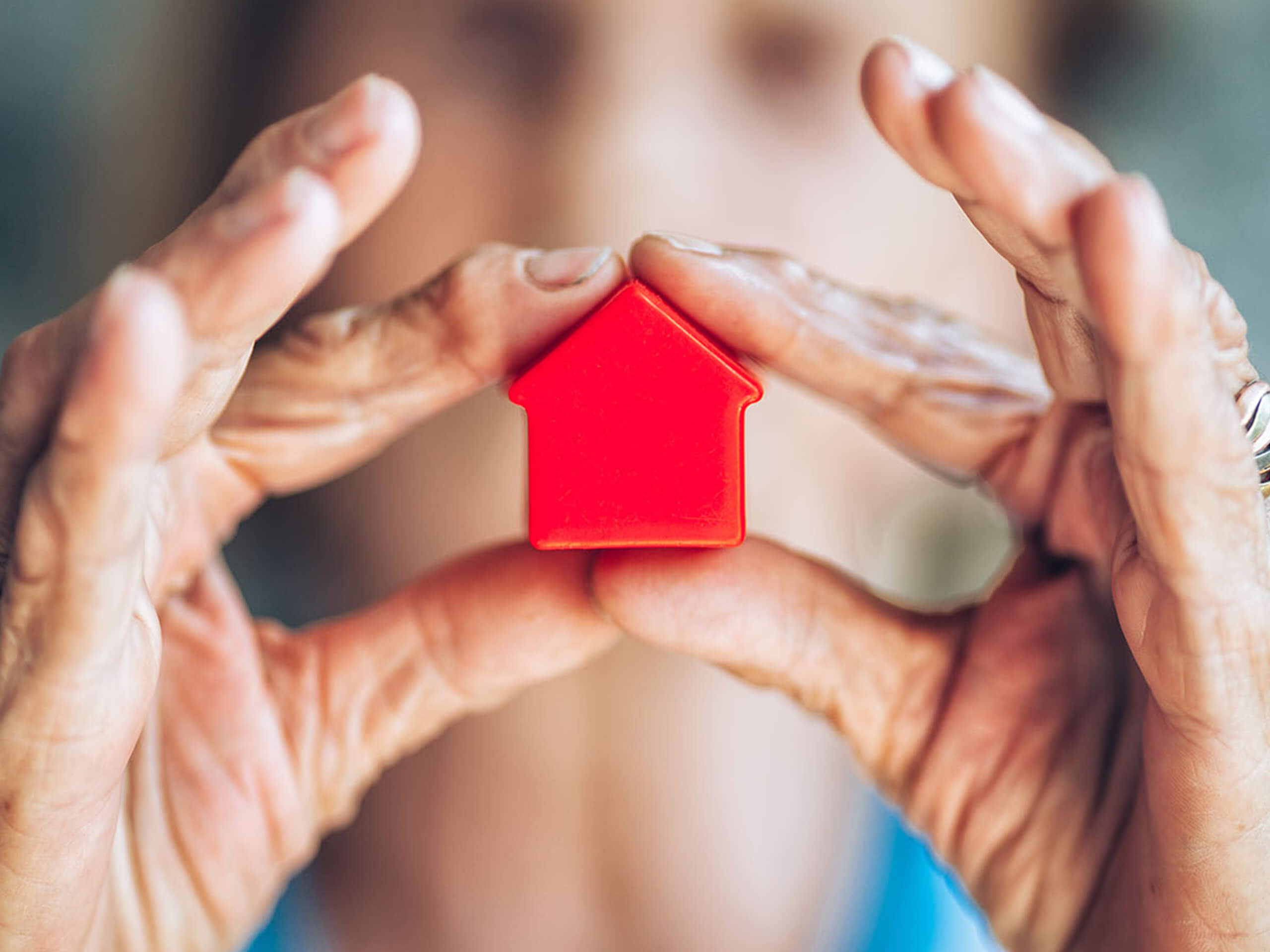 Ältere Frau hält ein rotes Modellhaus in den Händen als Symbol für die Vermietung von Immobilien