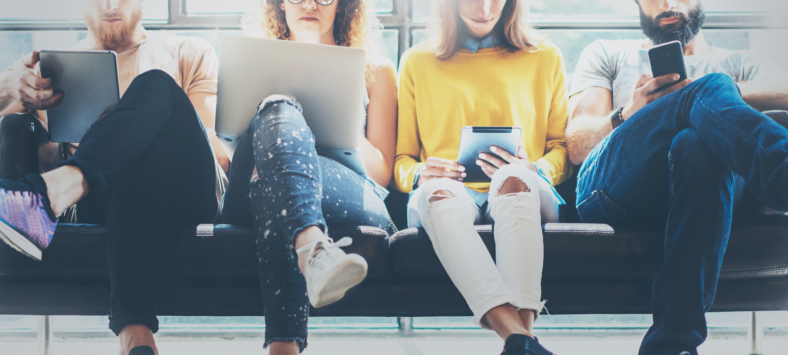 Online Marketing: Personen sitzen mit Laptop, Tablet und Smartphone auf einer Bank