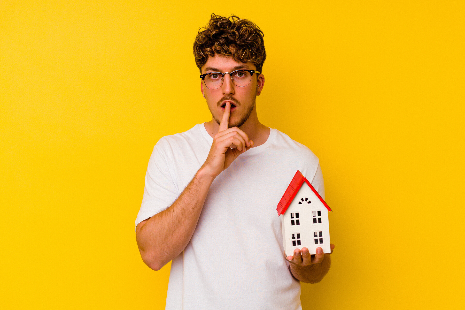 Mann macht Leise-Geste mit Modellhaus