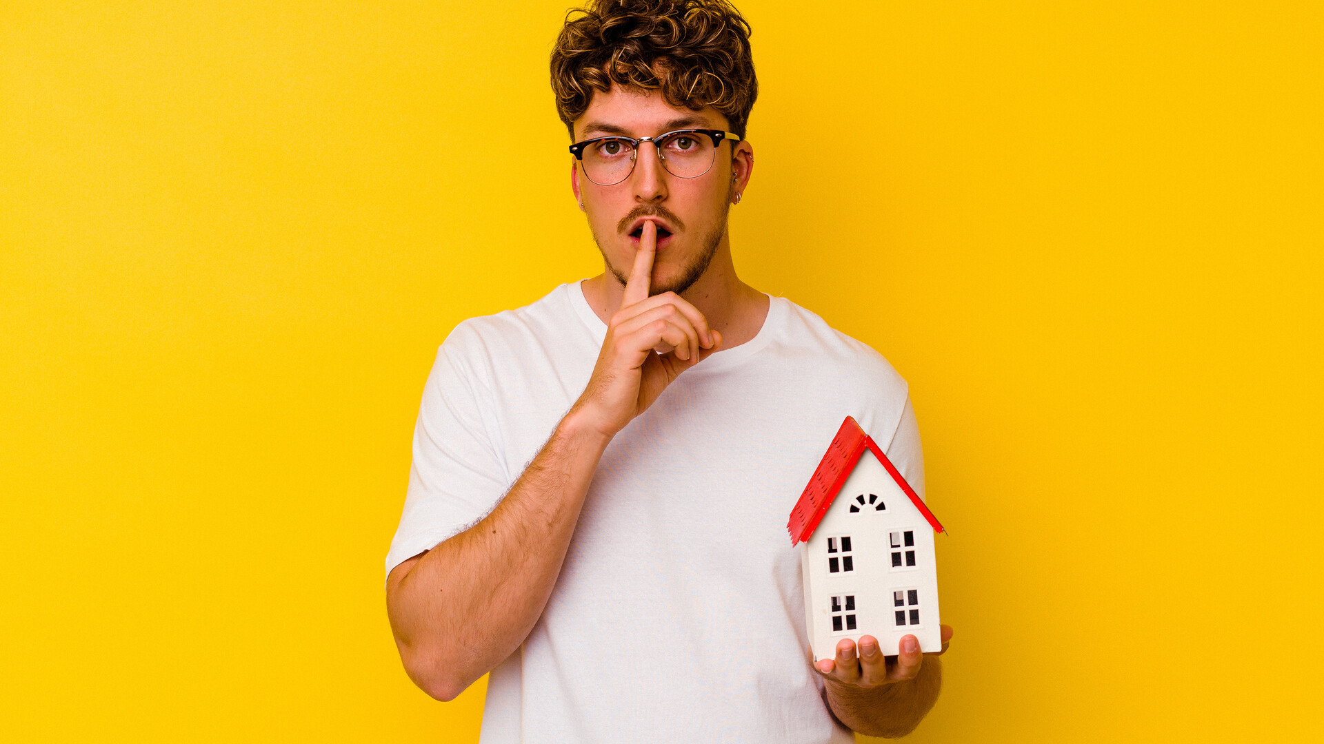 Mann macht Leise-Geste mit Modellhaus