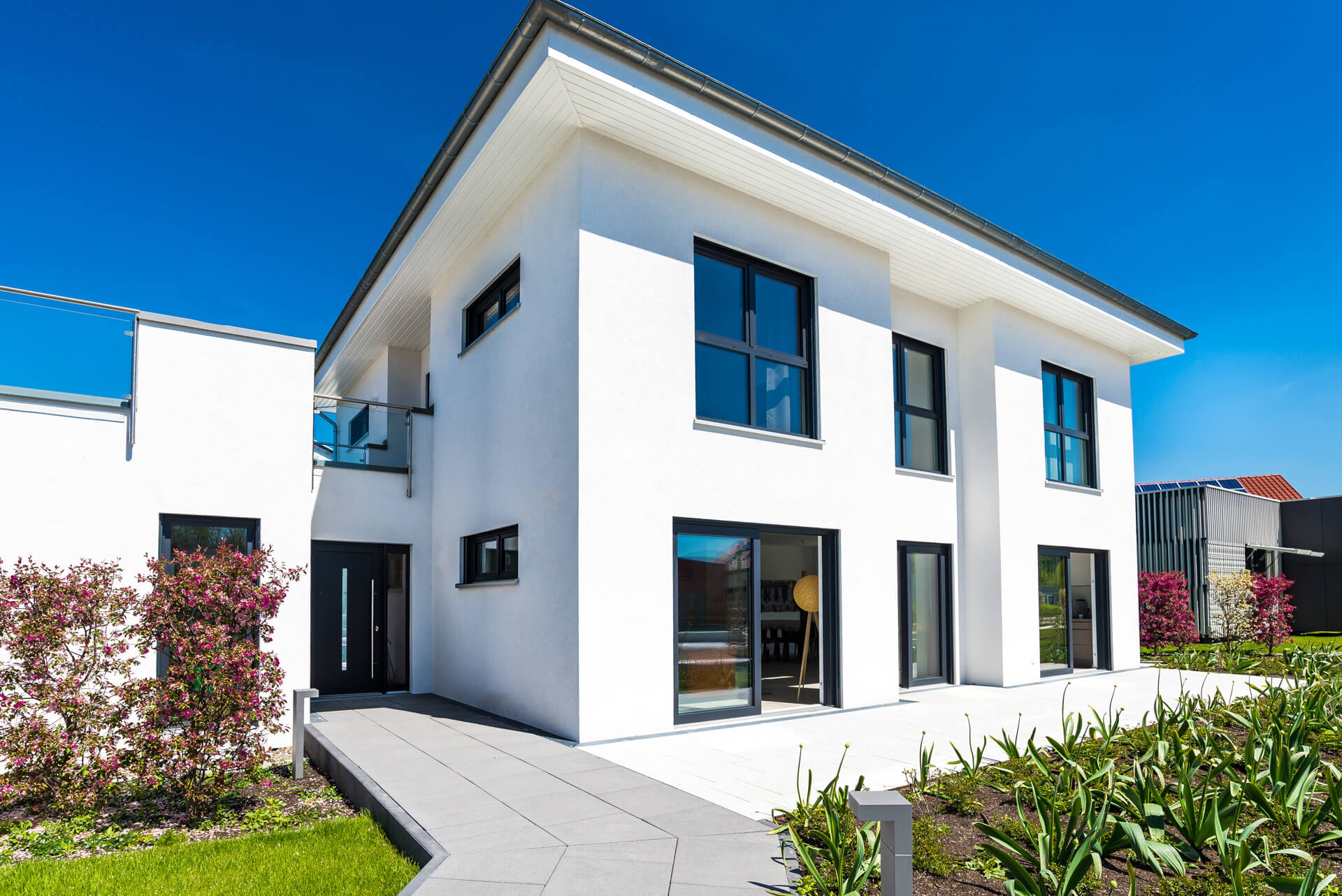 Weißes Haus mit großen Fenstern, Garten und blauem Himmel.