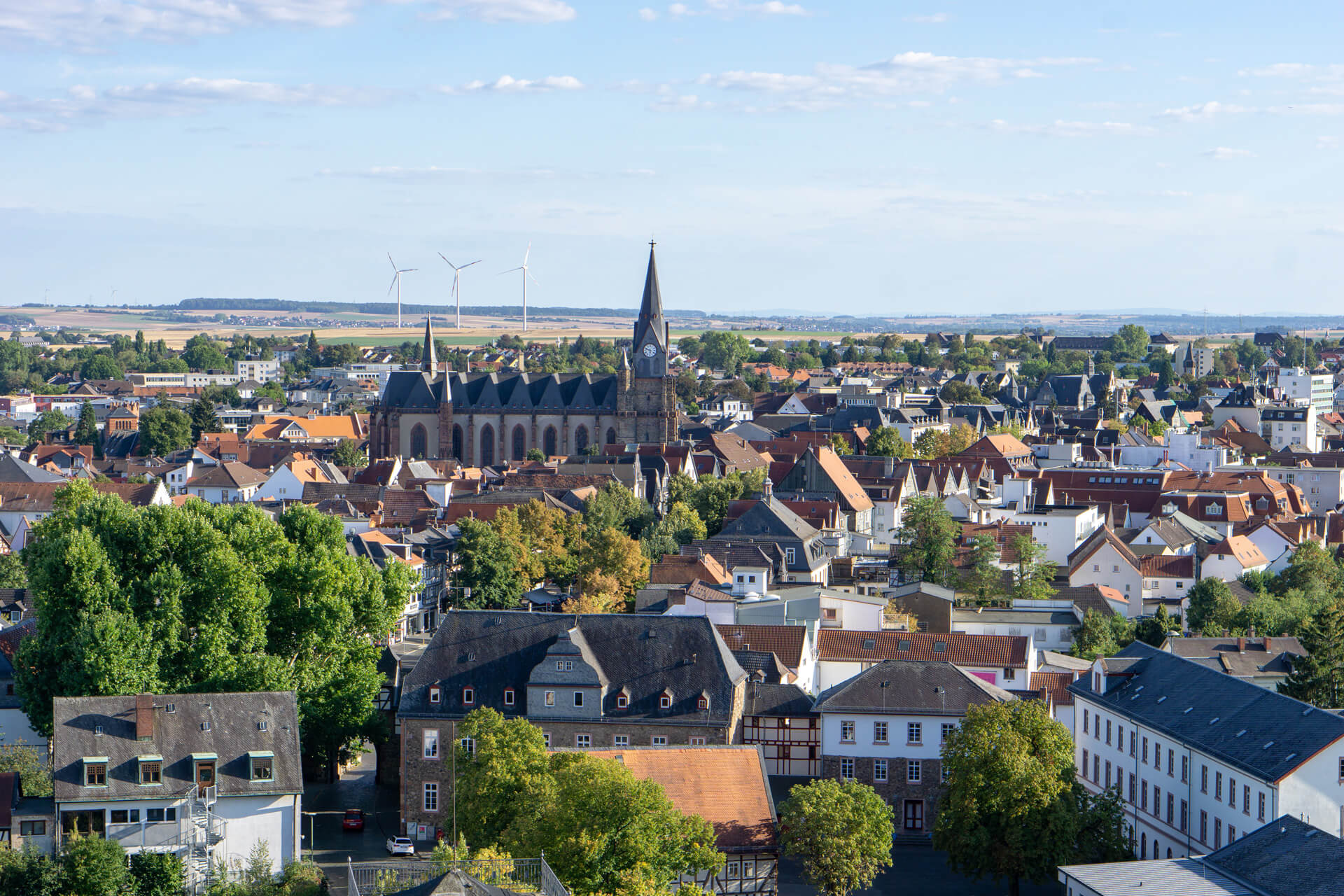 Kleinstadt mit Kirche, roten Dächern und Windrädern im Hintergrund.