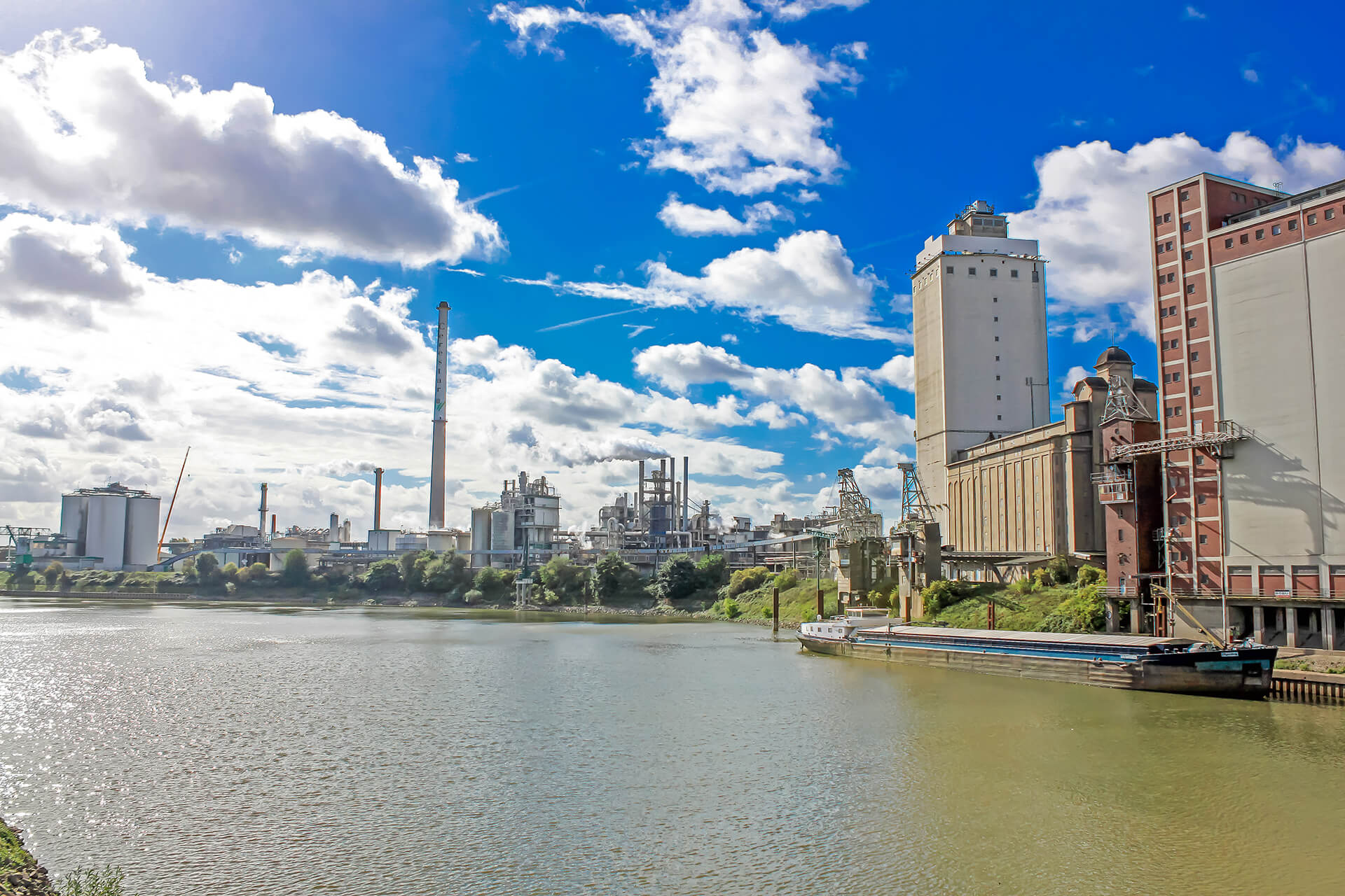 Fabriken am Flussufer unter blauem Himmel mit Wolken.