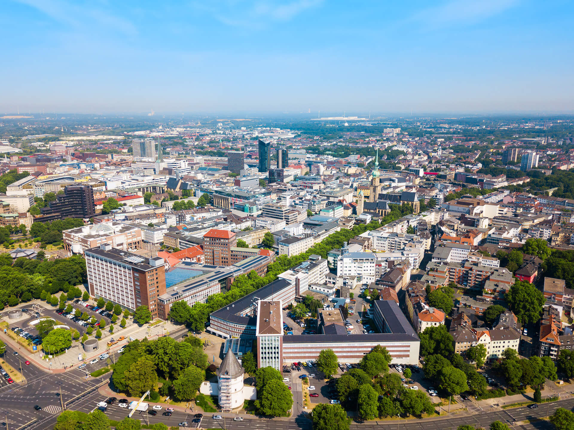 Stadt mit modernen Gebäuden, Straßen und Bäumen unter blauem Himmel.