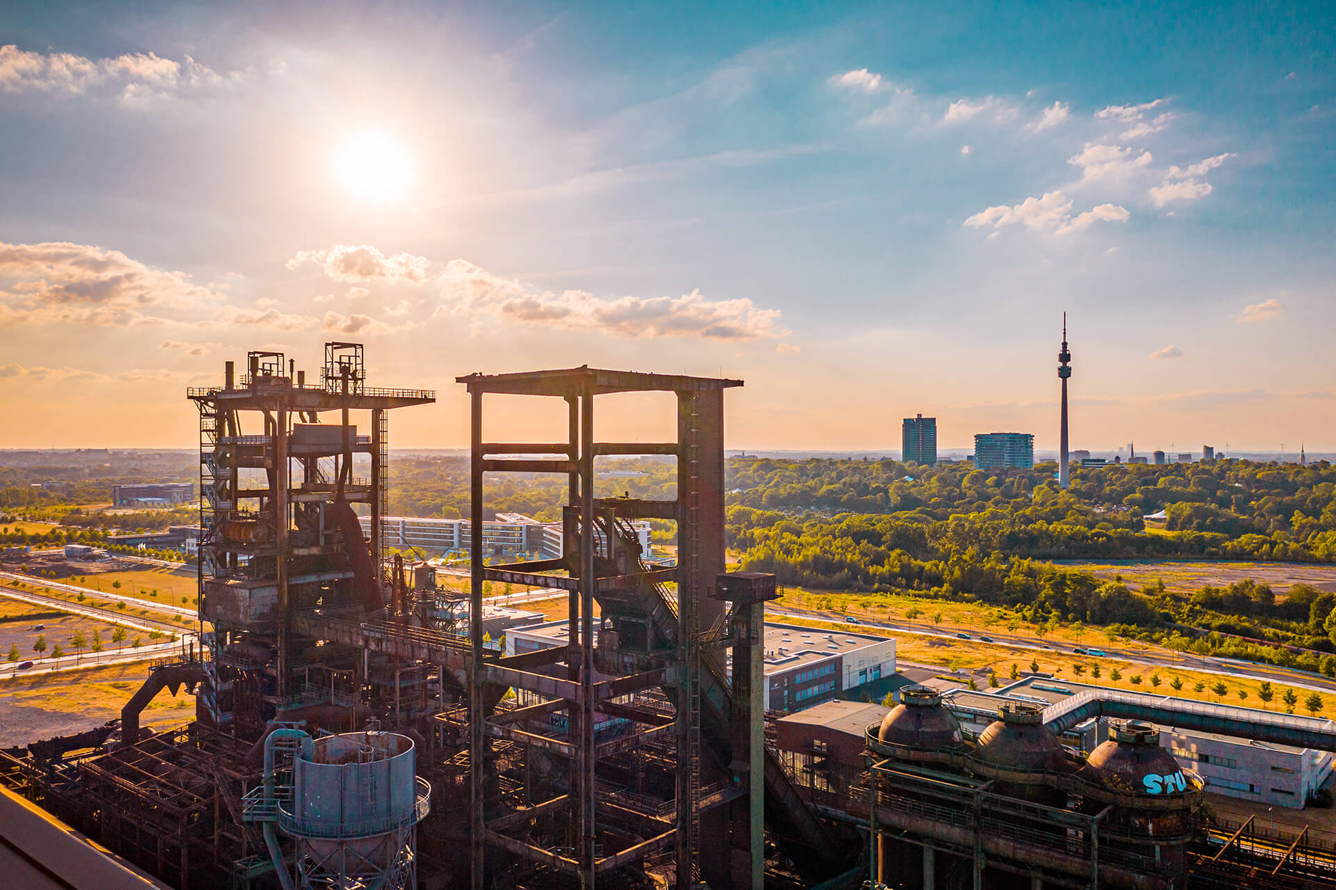 Industrieruine mit Metallgerüsten, Sonne, Stadt und Bäumen.