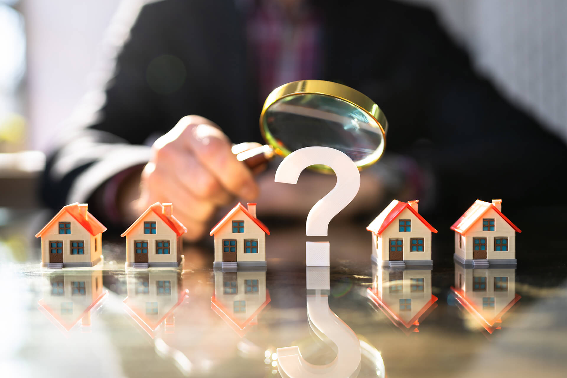 Lupe über Fragezeichen und Modellhäuser auf dem Tisch.
