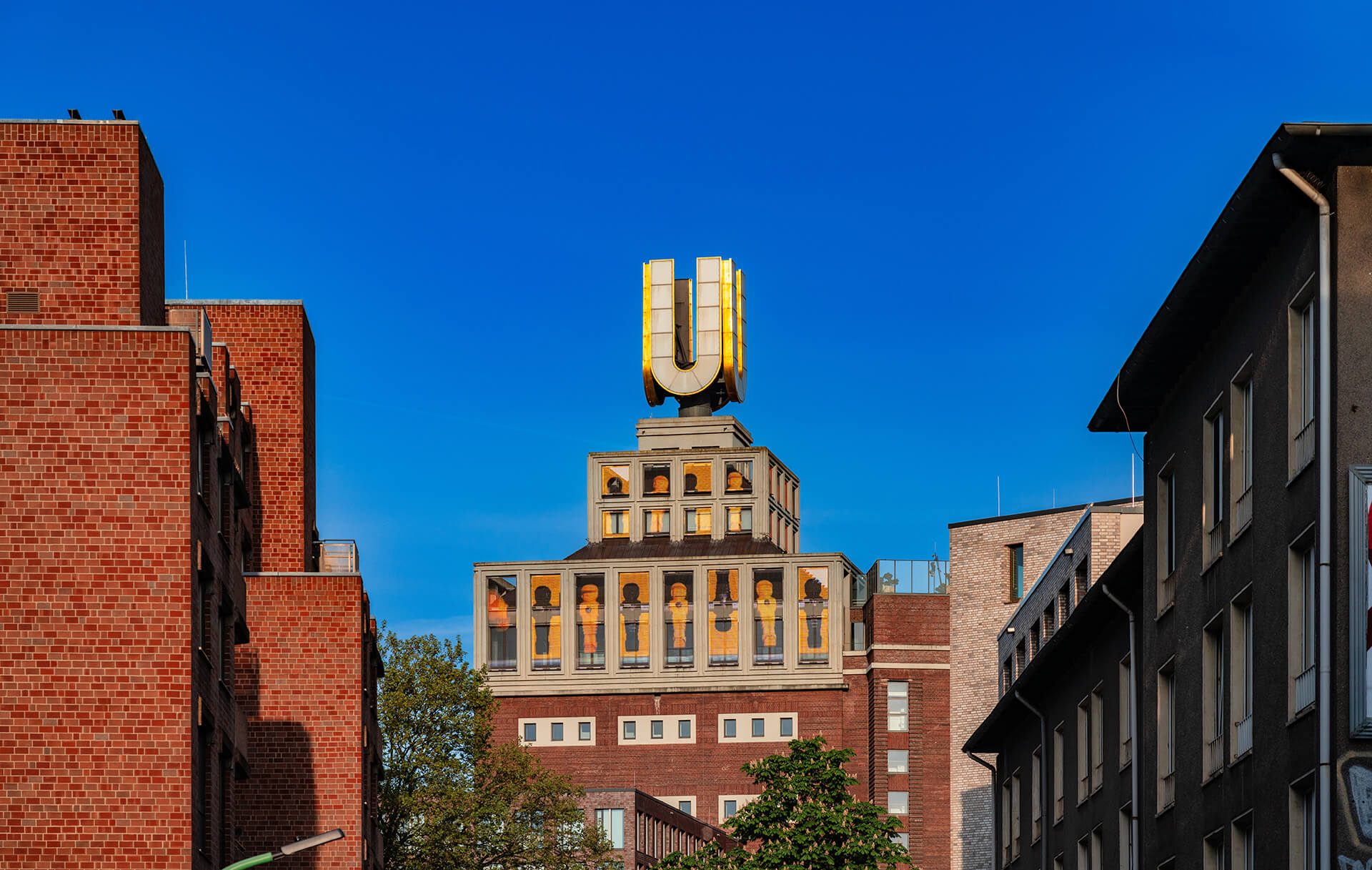 Backsteinbau mit großem gelben U auf dem Dach, klarer Himmel.