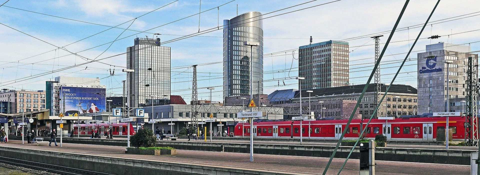 Rote Züge an Bahnsteigen, moderne Hochhäuser im Hintergrund.