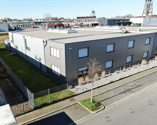 Graues Industriegebäude mit Zaun, umgeben von anderen Bauten.