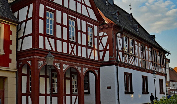 Fachwerkhaus mit weißen Wänden, roten Balken, bewölktem Himmel.