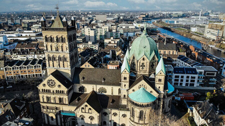 Kirche mit grünen Kuppeln in Flussnähe, teils bewölkter Himmel.