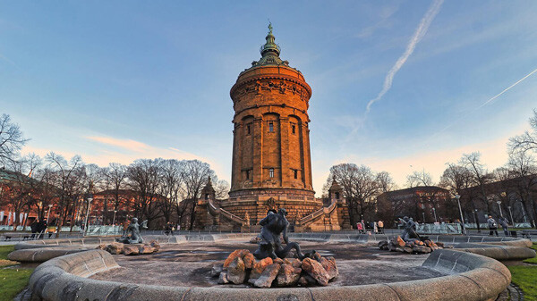 Historischer Steinturm hinter Brunnen mit Statuen bei Sonnenuntergang.
