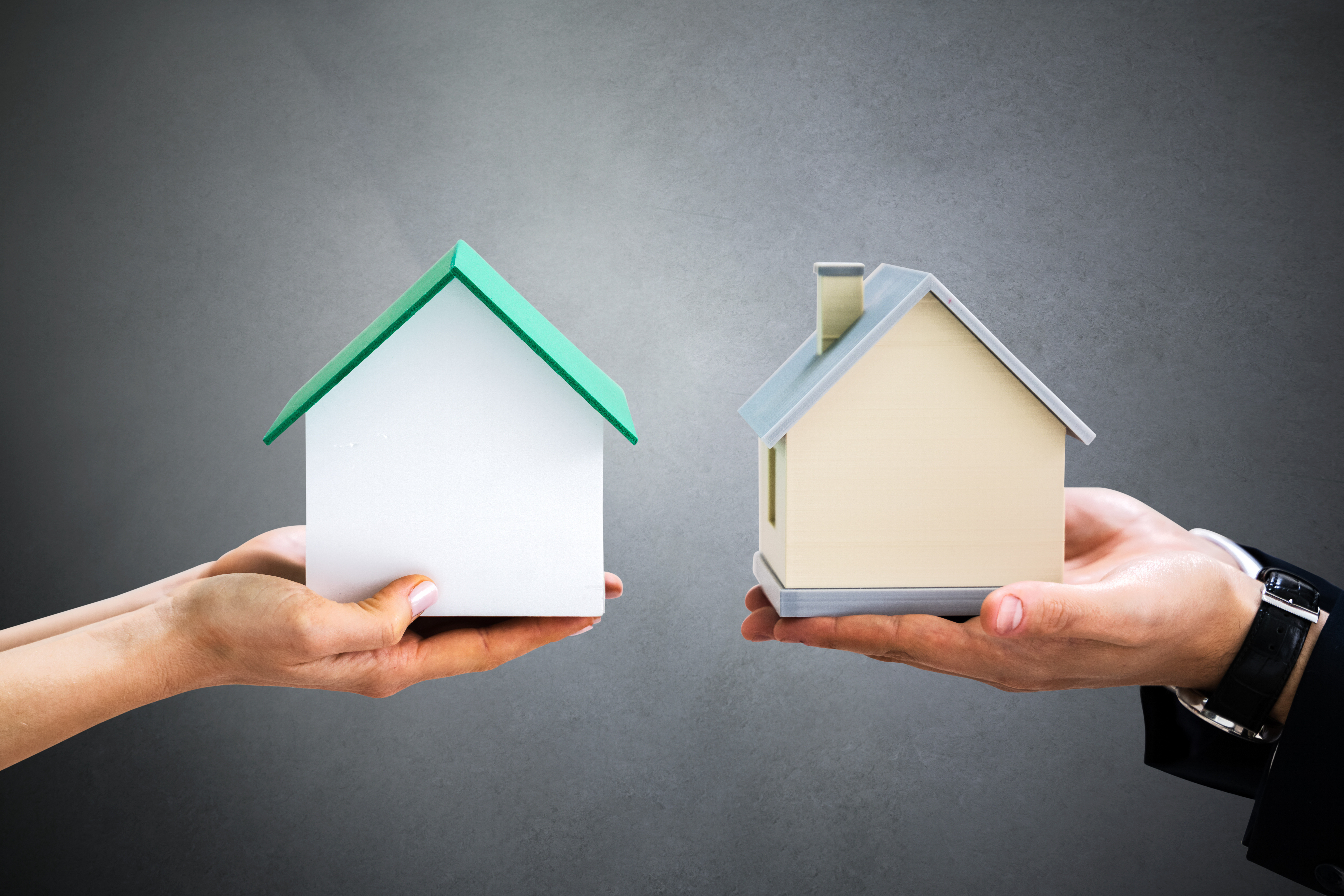 Zwei Hände tauschen Modellhäuser aus: Immobilientausch