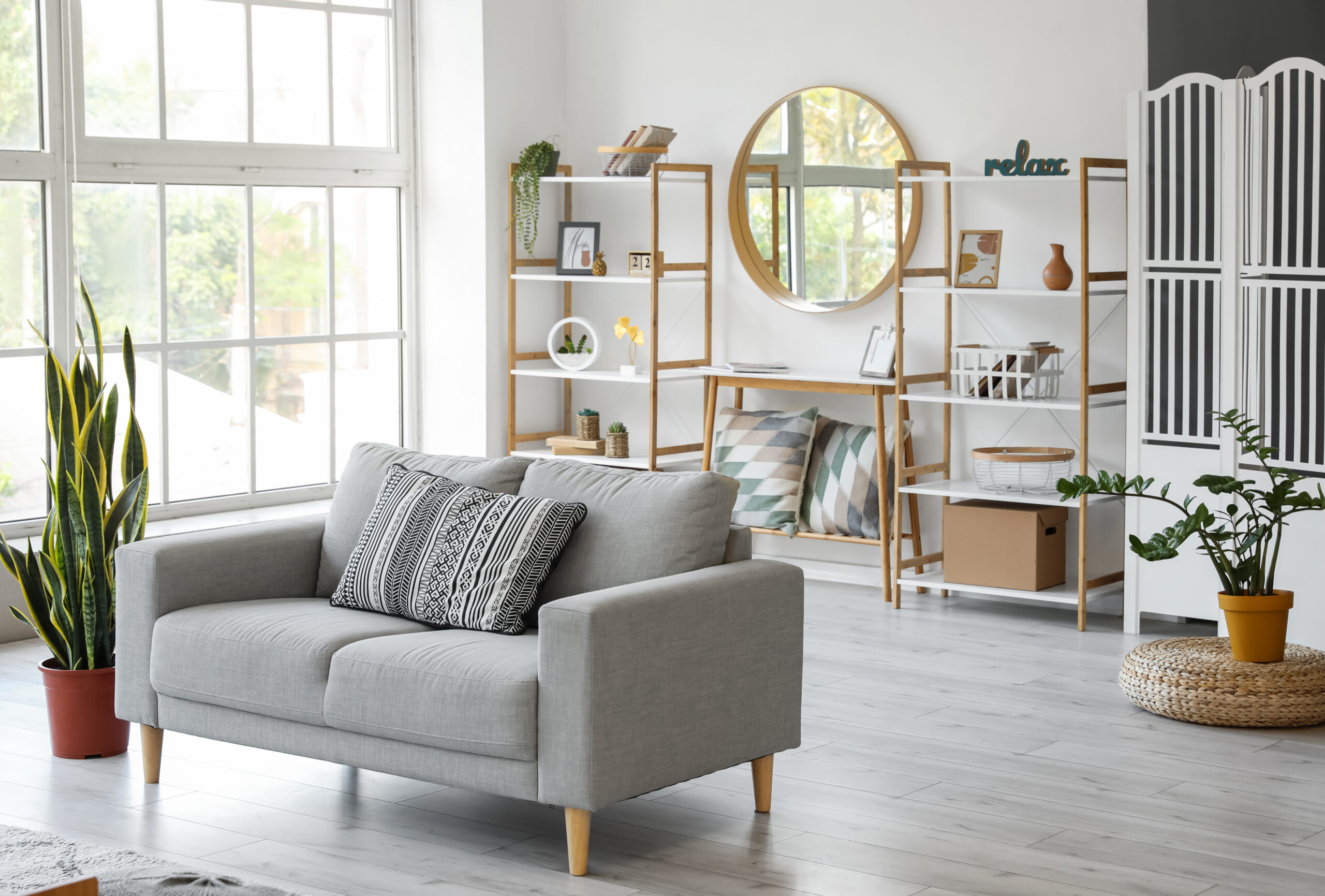 Moderne Wohnung: Graues Sofa, Pflanzen, Regale, runder Spiegel, großes Fenster.