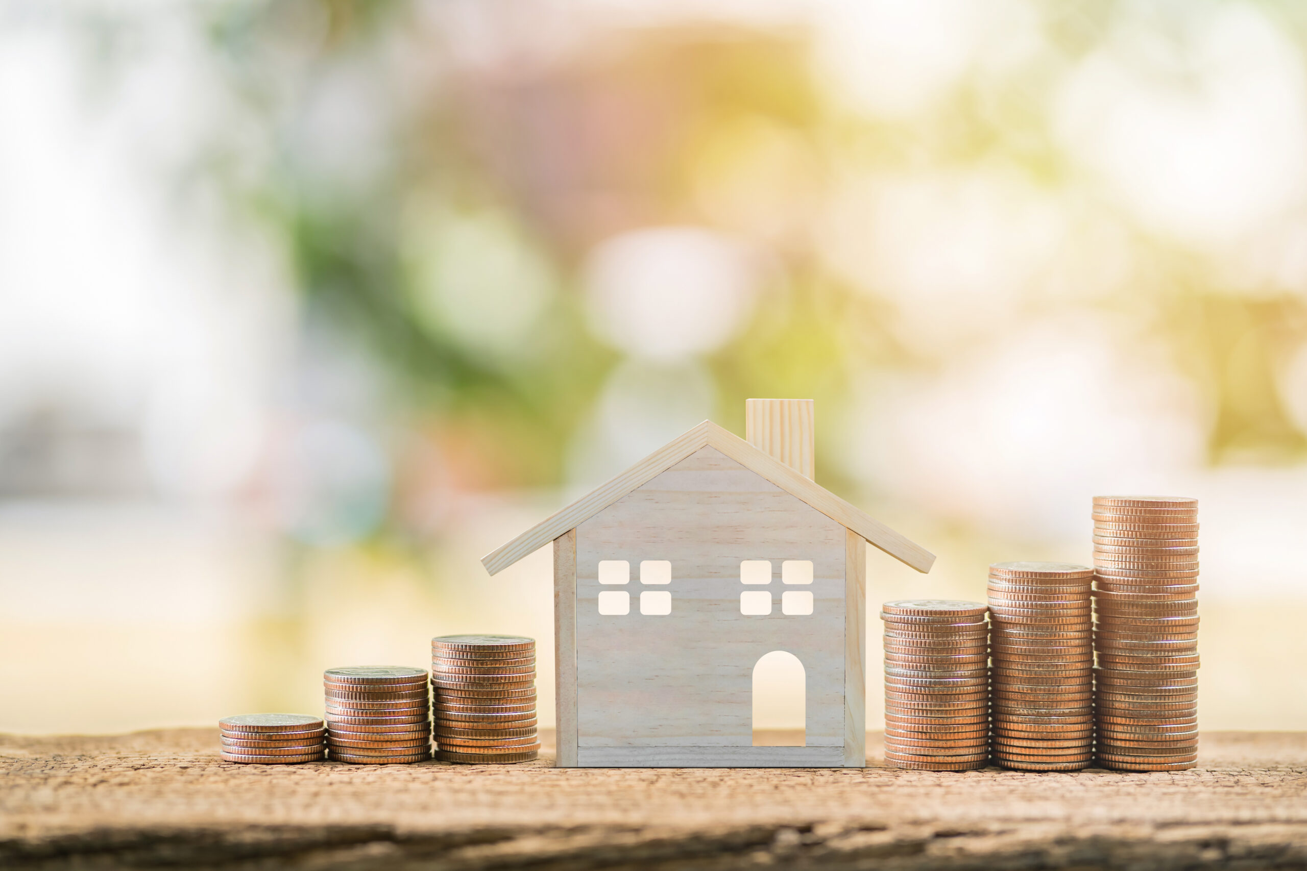 Hausmodell mit ansteigenden Münzstapeln auf beiden Seiten, Symbol für Anlageimmobilien