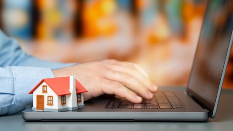 Mann tippt am Laptop, daneben ein Modellhaus