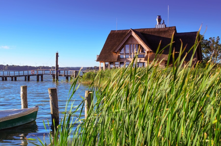 Strohgedecktes Haus am Hemmlsdorfer See, hohes Gras und Steg.