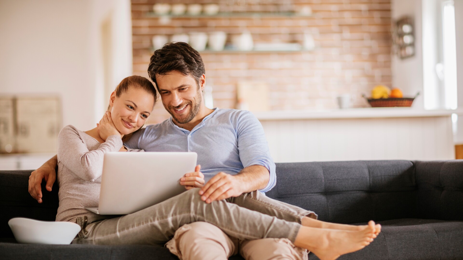 Lächelndes Paar auf der Couch, das gemeinsam auf einen Laptop schaut