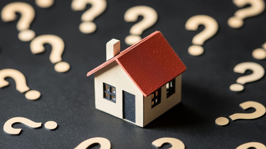 Kleines Modellhaus mit Holzfragezeichen auf dunklem Hintergrund.