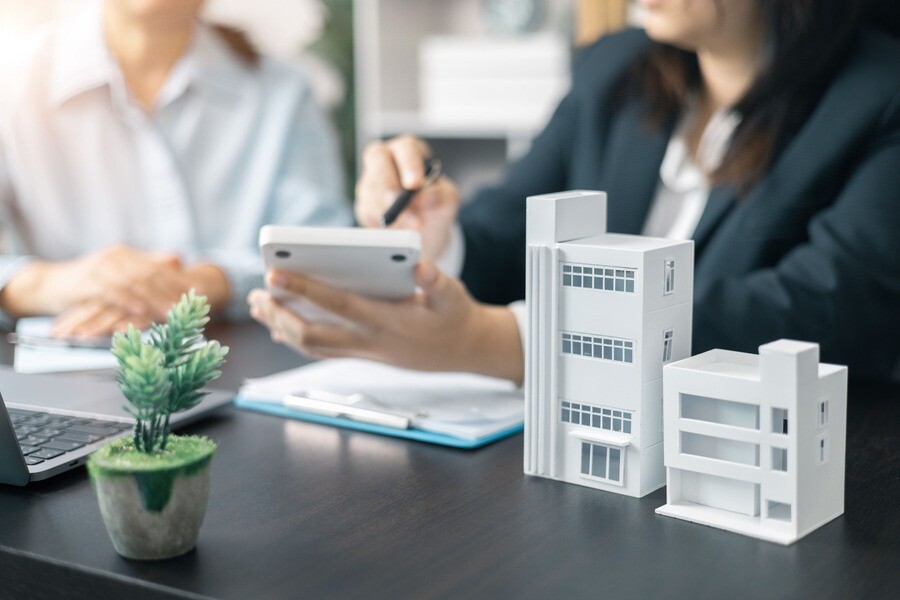 Zwei Personen besprechen Unterlagen am Schreibtisch mit Hausmodellen