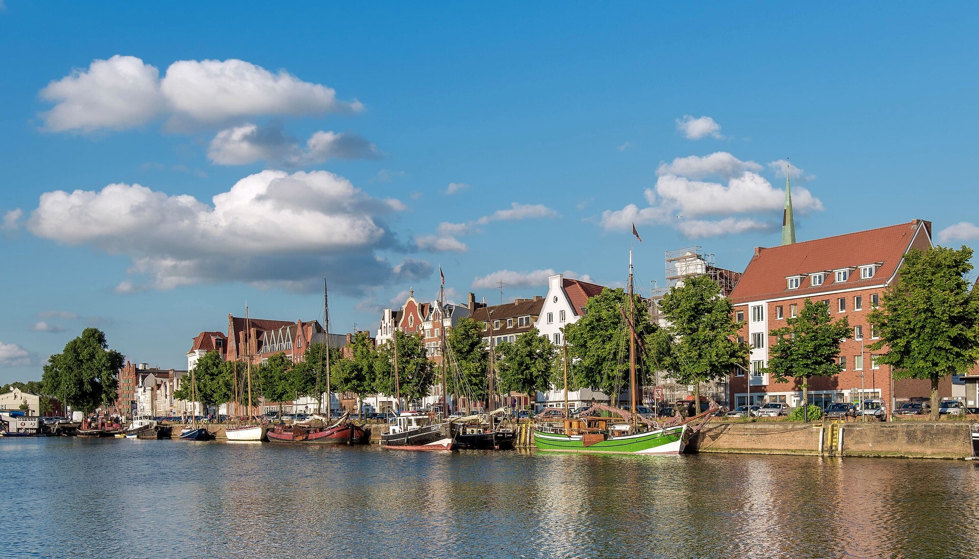 Boote am Ufer mit Bäumen und roten Dächern unter blauem Himmel