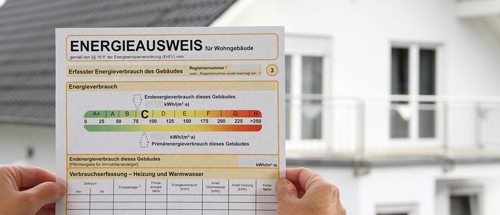 Mann hält Energieausweis vor Haus.