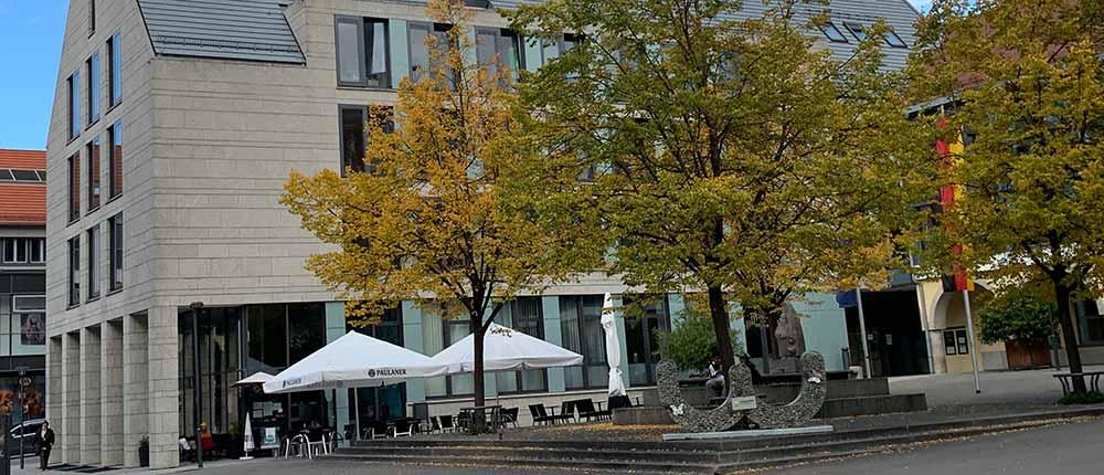 Modernes Steinhaus am Rathausplatz Hagen mit Außengastronomie und herbstlichen Bäumen.