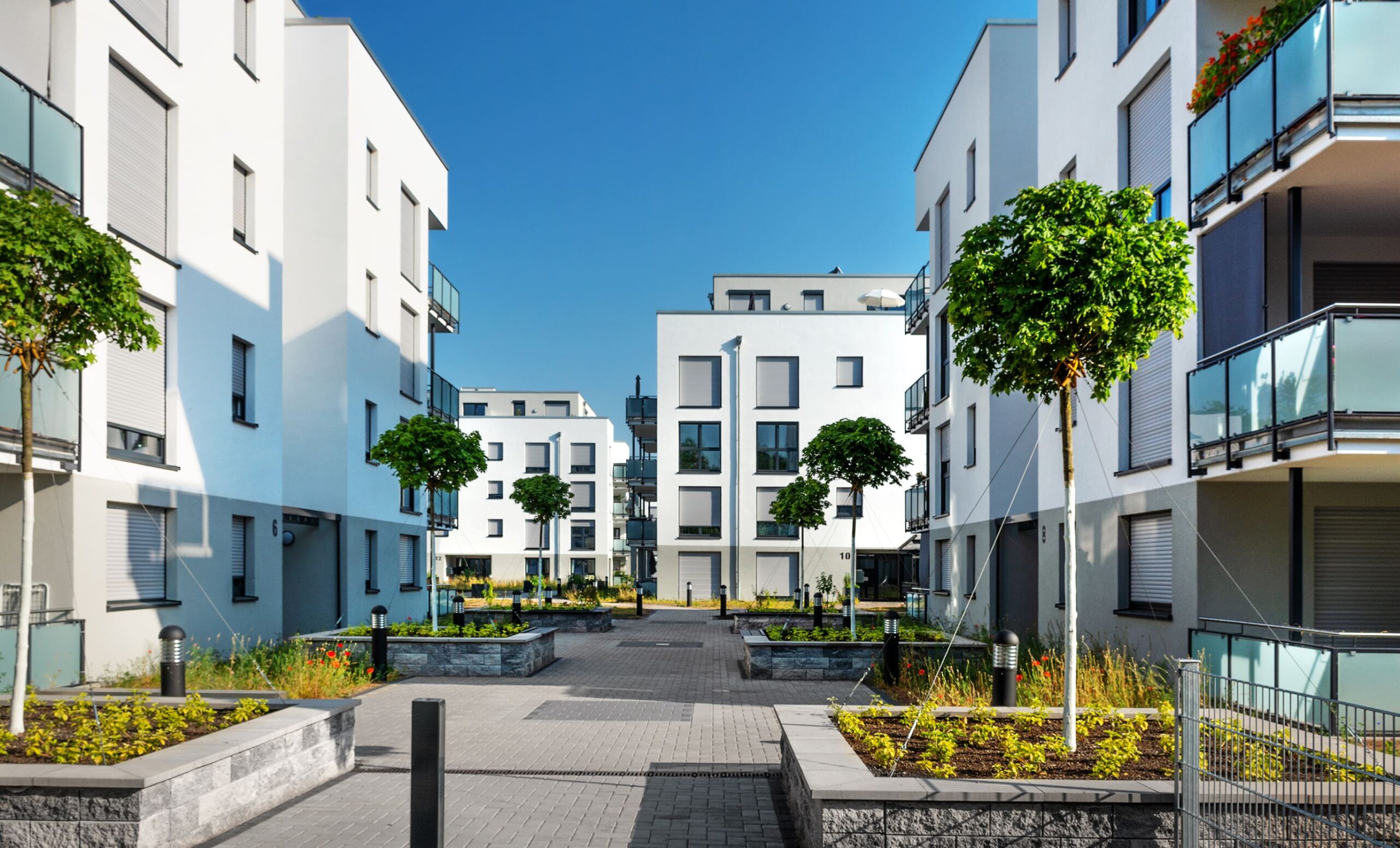 Moderne weiße Wohnanlage mit begrüntem Innenhof und Balkonen.