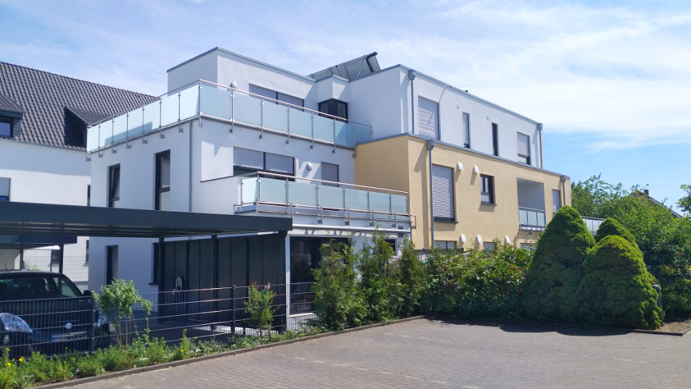 Modernes Mehrfamilienhaus mit großen Balkonen und Carport.