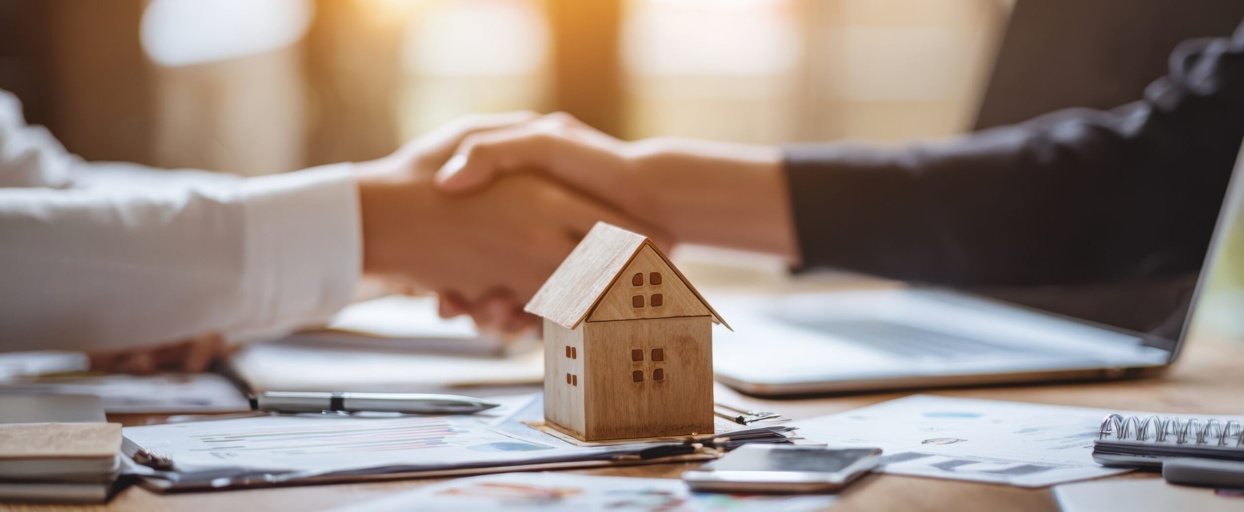 Erfolgreiches Immobiliengeschäft: Händedruck über einem Holzhaus-Modell.