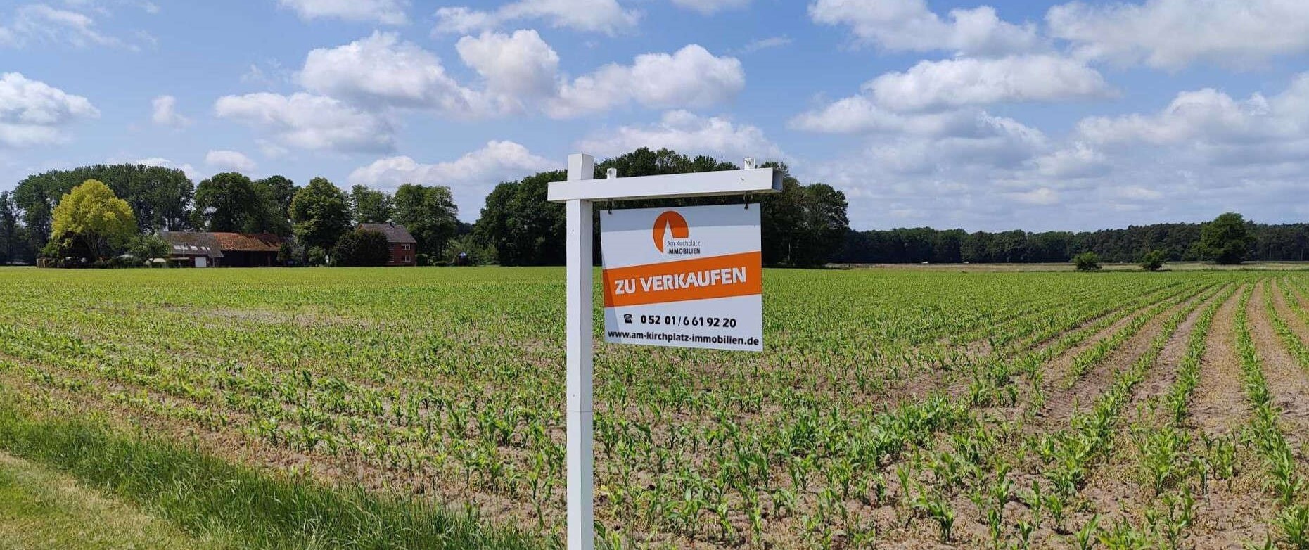 Schild "Zu verkaufen" auf einem Feld mit Kontaktdaten vom Am Kirchplatz Immobilien