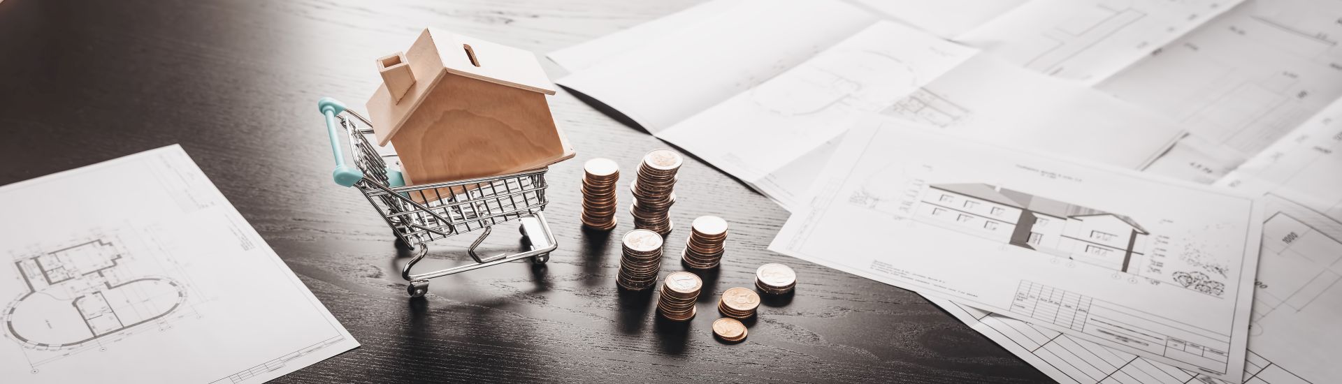 Modellhaus in einem Einkaufswagen mit Münzen und Unterlagen auf einem Tisch